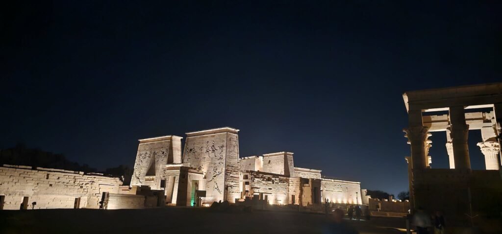Templo de Philae dedicado à deusa Ísis, Aswan, Egito, com turistas acompanhados de guia em português observando a arquitetura antiga. Contato WhatsApp: +201204128282 – Guia Viagem Egito.