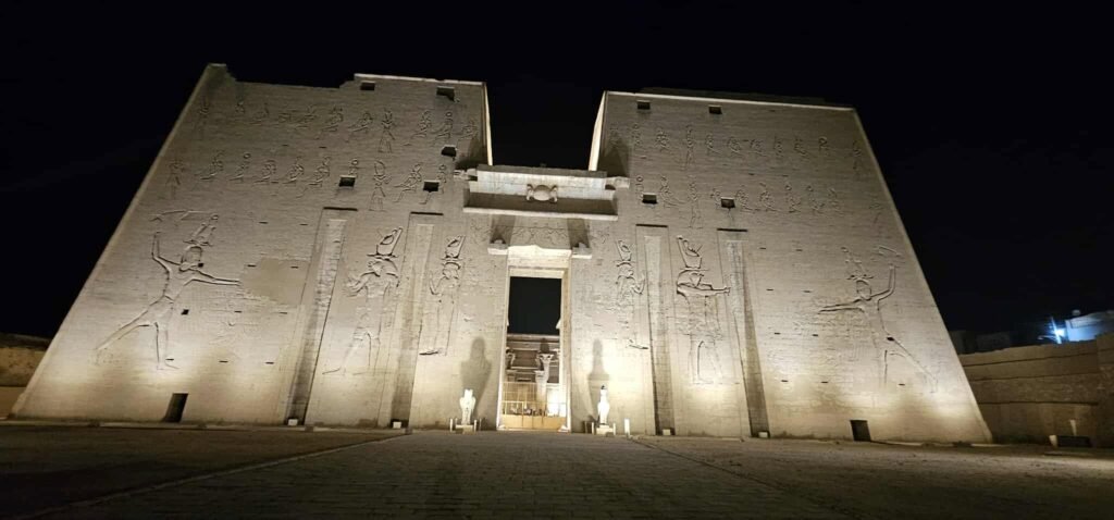 Templo de Edfu dedicado ao deus Hórus, Egito, com turistas acompanhados de guia em português admirando as paredes decoradas com hieróglifos e a arquitetura antiga
