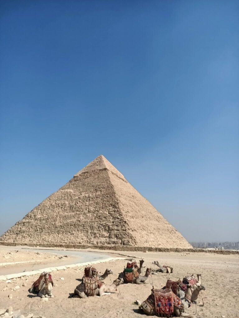Turistas visitando as Pirâmides de Gizé, Egito, acompanhados de guia em português, observando a grandiosa arquitetura antiga