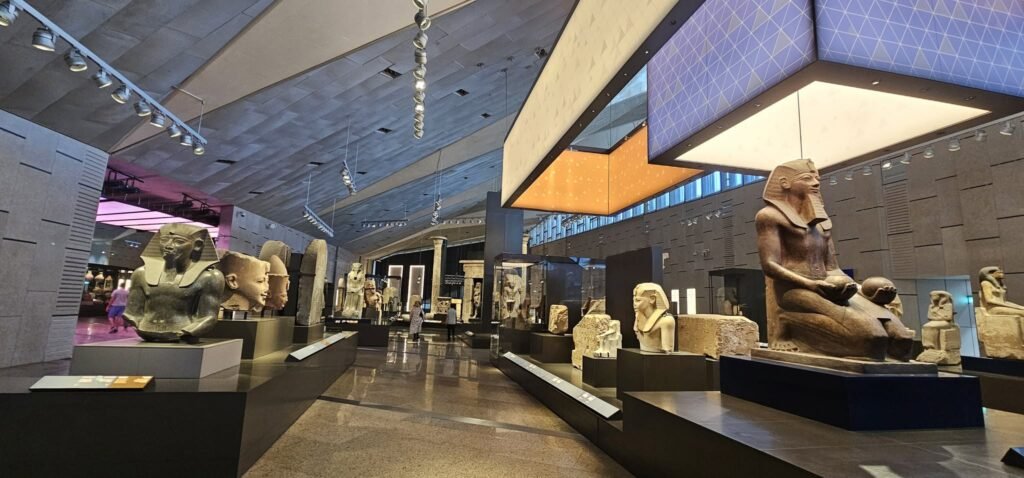 Visitantes explorando o Grande Museu Egípcio (GEM) no Cairo, Egito, acompanhados de guia em português. Contato WhatsApp: +20 120 412 8282 – Guia Viagem Egito