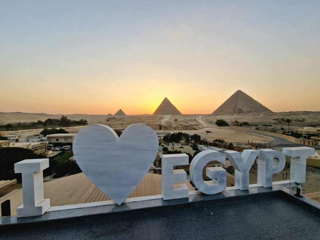 Rooftop tradicional com mesas decoradas para jantar ao pôr do sol, oferecendo vista frontal das Pirâmides de Gizé, experiência gastronômica única com culinária egípcia