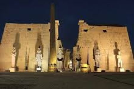 Vista noturna do Templo de Luxor iluminado, com colunas monumentais e obelisco na entrada